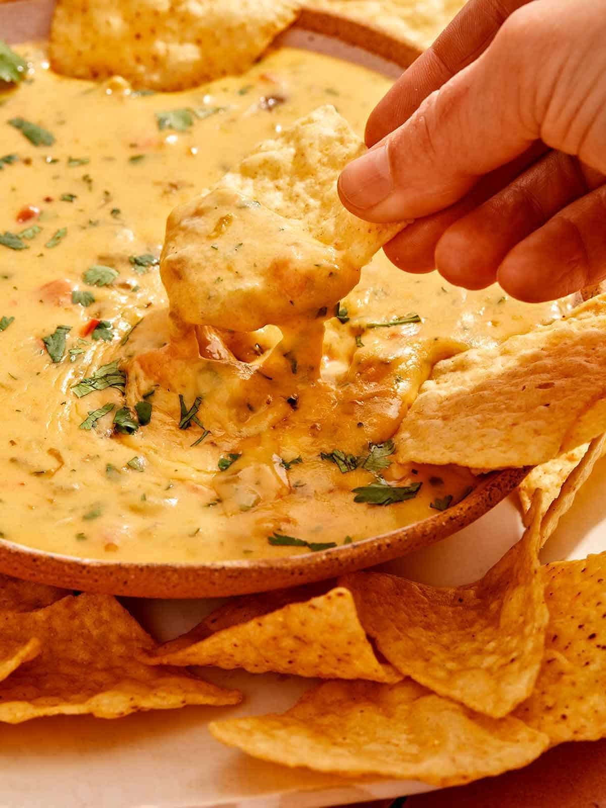 A hand dipping a chip in queso that is in a bowl.