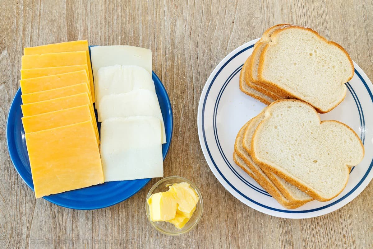 ingredients for easy baked grilled cheese sandwiches including cheese slices, butter and white bread slices