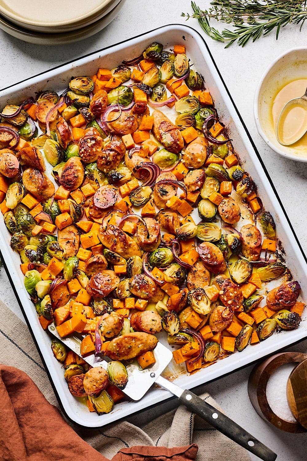 sheet pan sausage with sweet potatoes, brussels sprouts, red onion with spatula.