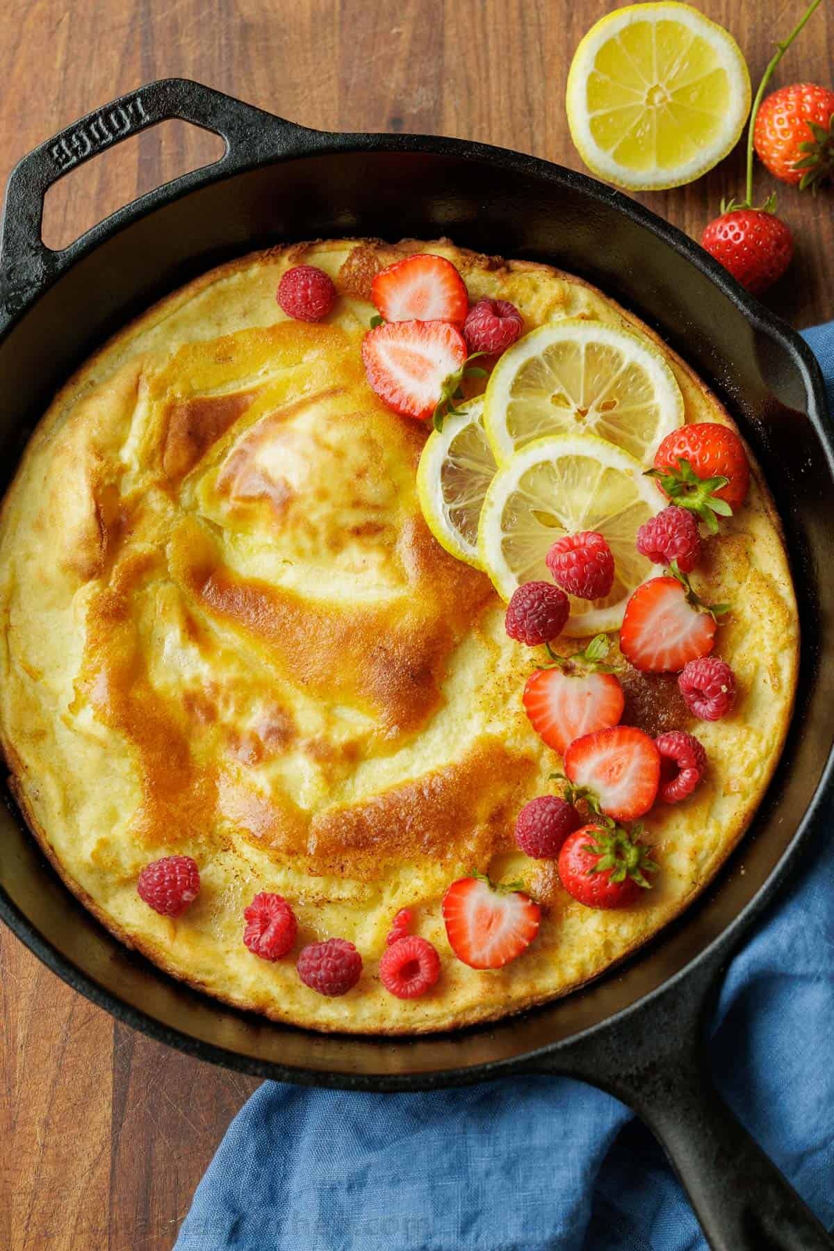 Sourdough Dutch Baby pancake recipe in a cast iron pan topped with lemon slices and sliced strawberries