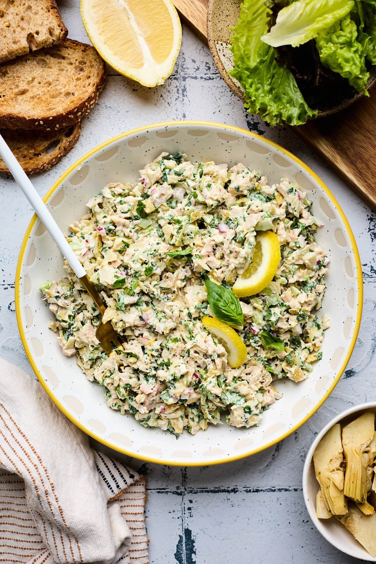 spinach artichoke chicken salad in bowl with lemon wedge, basil, and fork.
