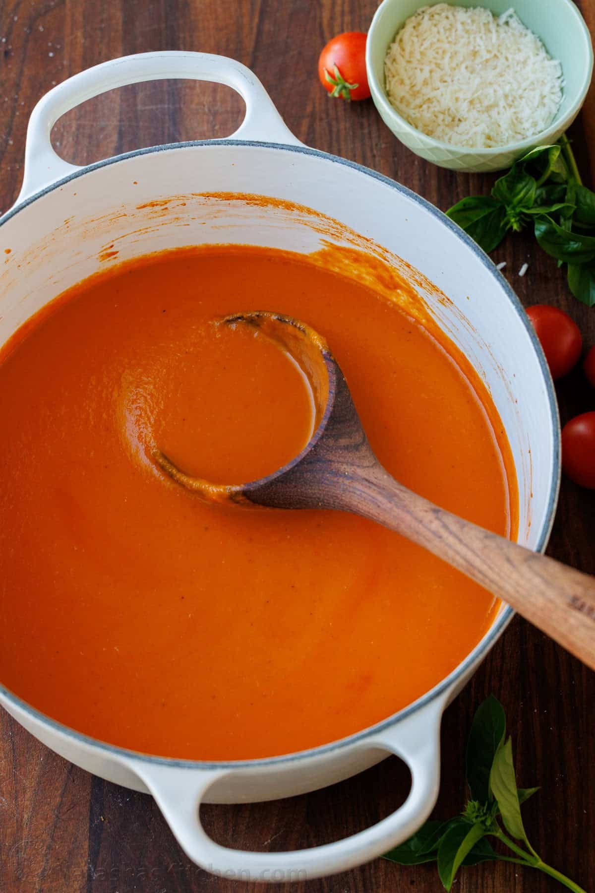 Red broth in a white Dutch Oven with a wooden spoon
