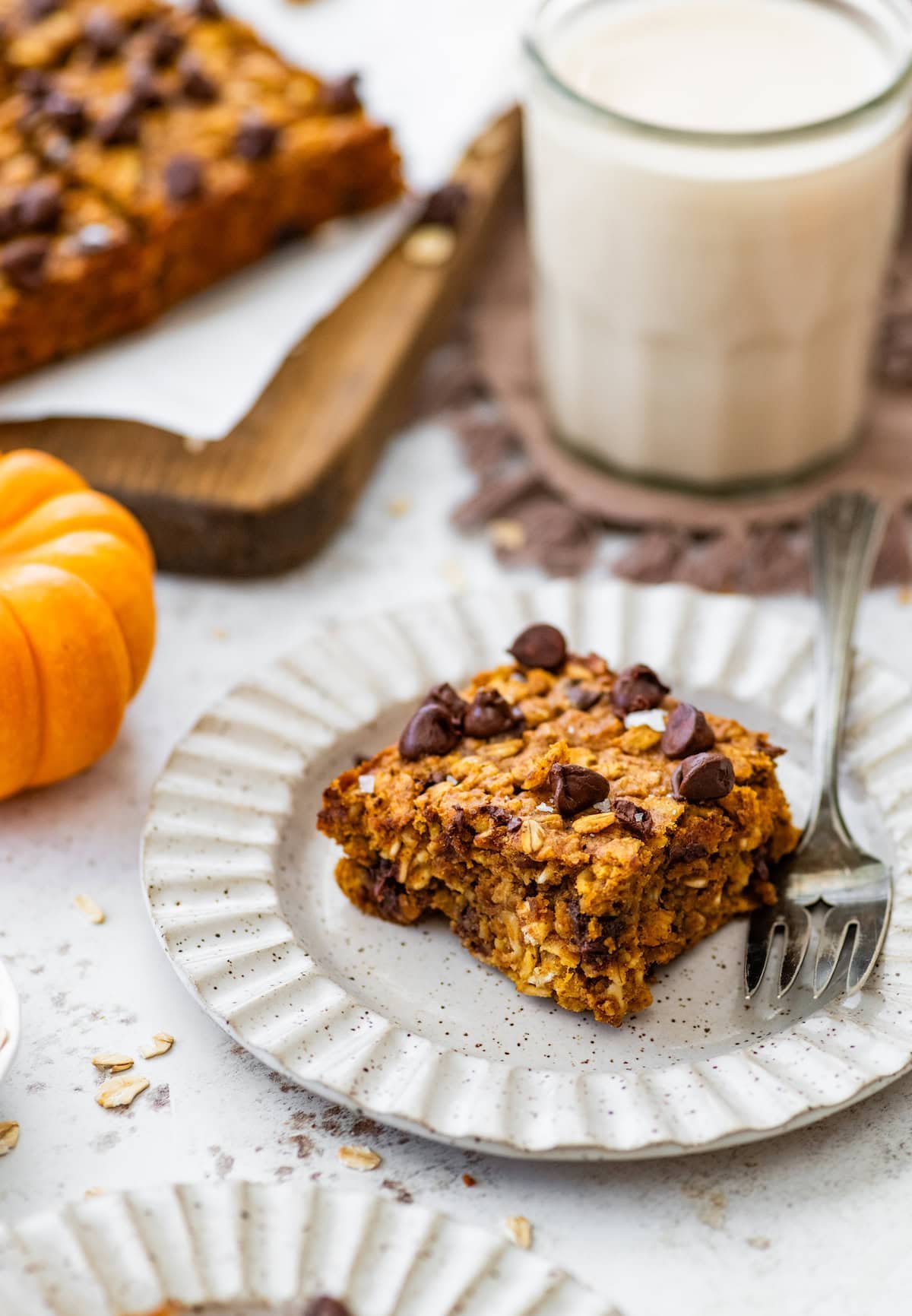 piece of pumpkin chocolate chip oatmeal bar on plate with fork and glass of milk.