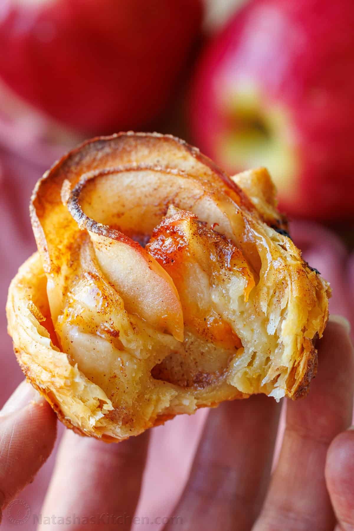 Easy Apple roses taste just like classic apple pie, but look festive and beautiful! Tey are easy to make and perfect as a holiday dessert. a bite taken out of an apple rose pastry