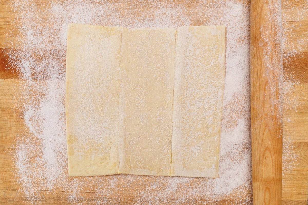 Easy Apple roses taste just like classic apple pie, but look festive and beautiful! Tey are easy to make and perfect as a holiday dessert. Puff pastry on a butcher block with flour dusted on the top