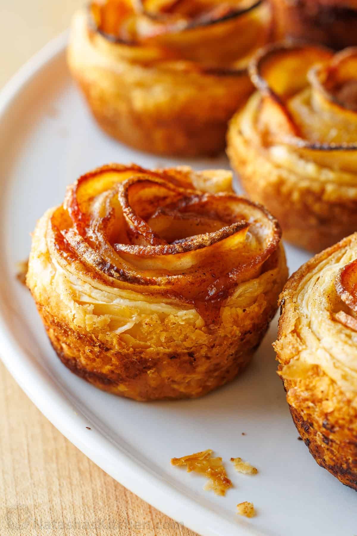 Easy Apple roses taste just like classic apple pie, but look festive and beautiful! Tey are easy to make and perfect as a holiday dessert. Apple roses recipe on a white plate with flakey puff pastry
