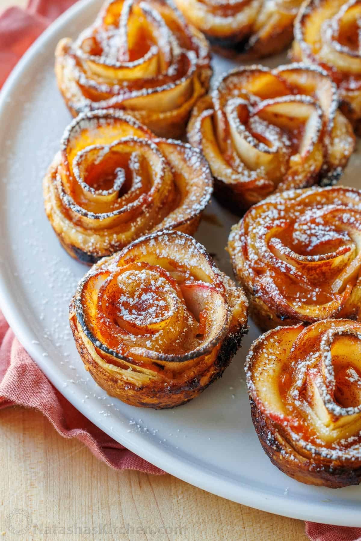 Easy Apple roses taste just like classic apple pie, but look festive and beautiful! Tey are easy to make and perfect as a holiday dessert. Plate of apple roses pastries with powdered sugar dusted on top
