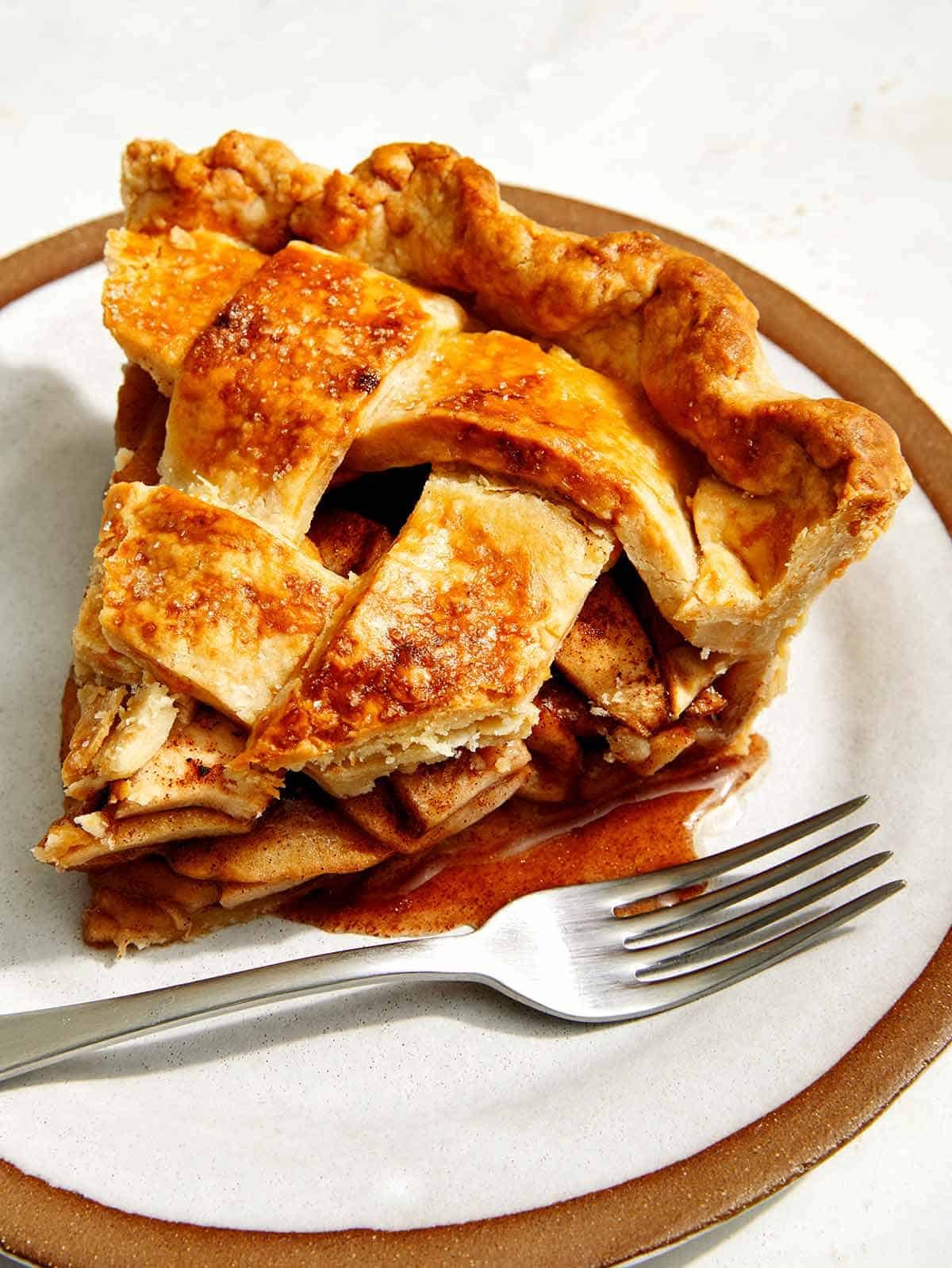 A slice of apple pie on a plate with a fork next to it.