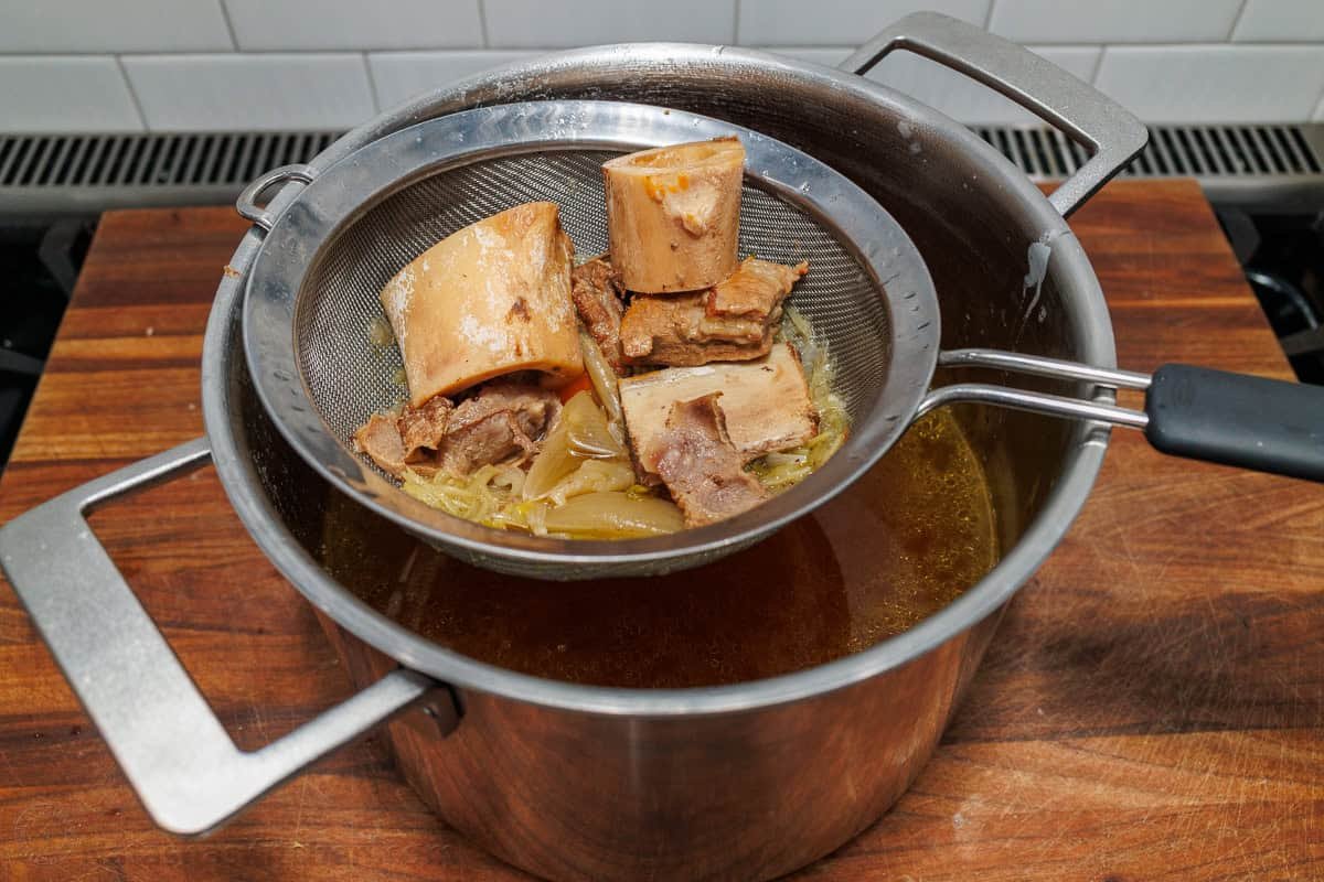 Straining beef bones and vegetables for beef stock