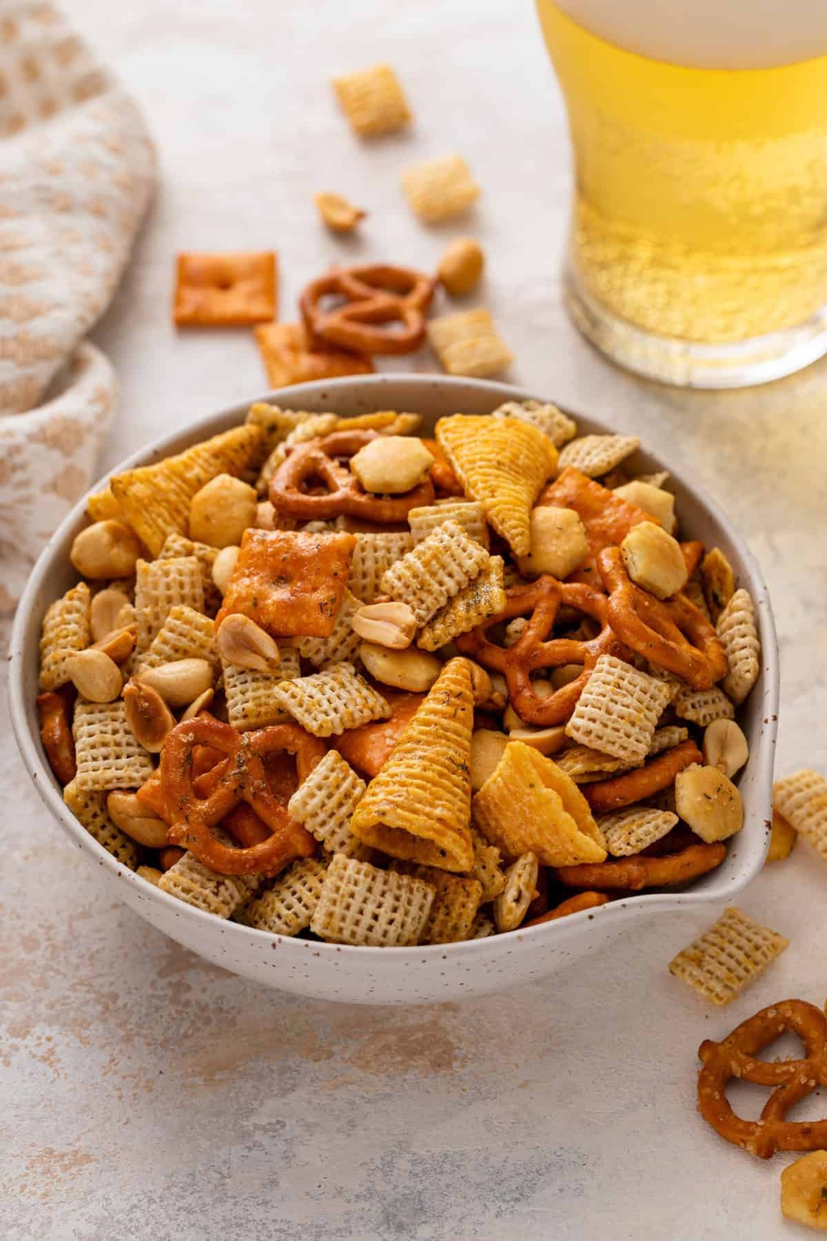 White bowl filled with ranch chex mix, with a beer in the background.