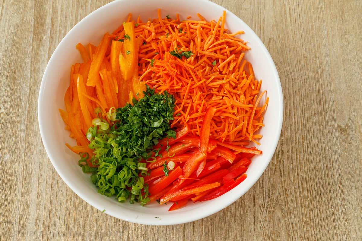 Spicy Korean Carrot Salad packs so much flavor into one crowd-pleasing side dish. The easy dressing melds the whole salad together in minutes. Shredded vegetables in a white bowl including peppers and herbs