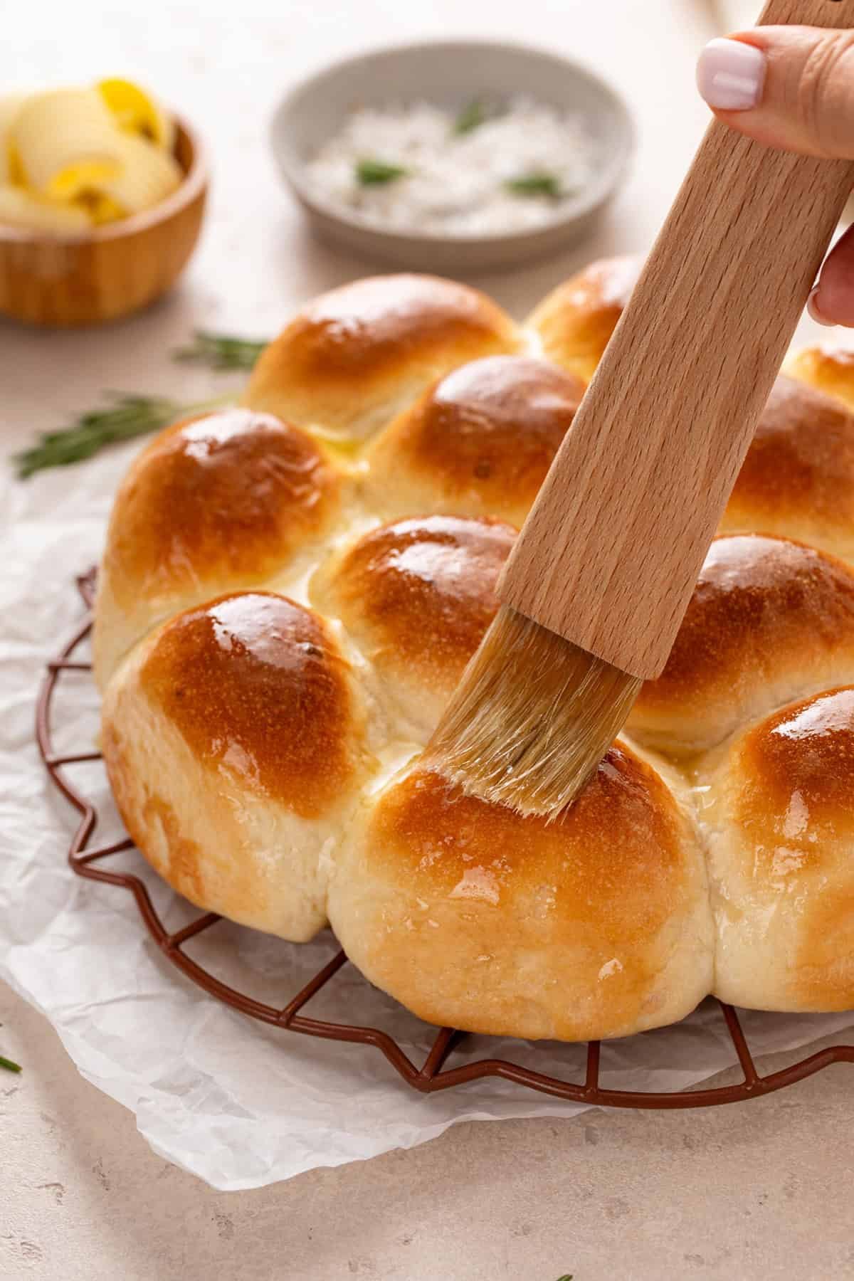 Melted butter being brushed on hot brown and serve dinner rolls.