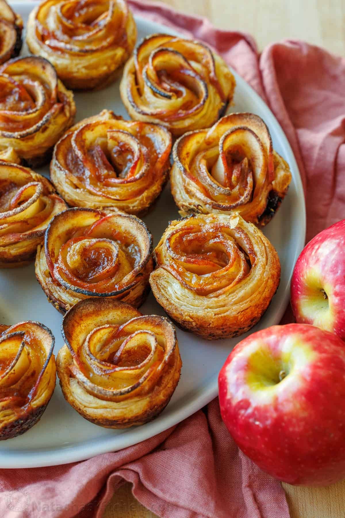 Easy Apple roses taste just like classic apple pie, but look festive and beautiful! Tey are easy to make and perfect as a holiday dessert. Apple roses lined up on a plate with two apples