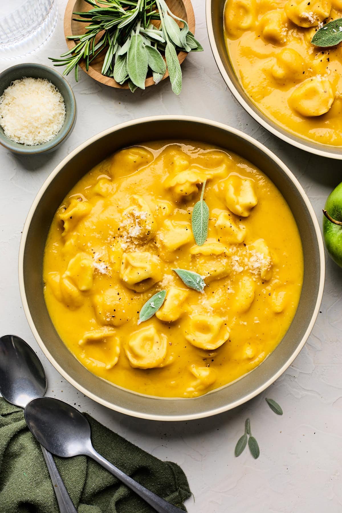 butternut squash tortellini soup in bowl with sage leaves and Parmesan cheese.