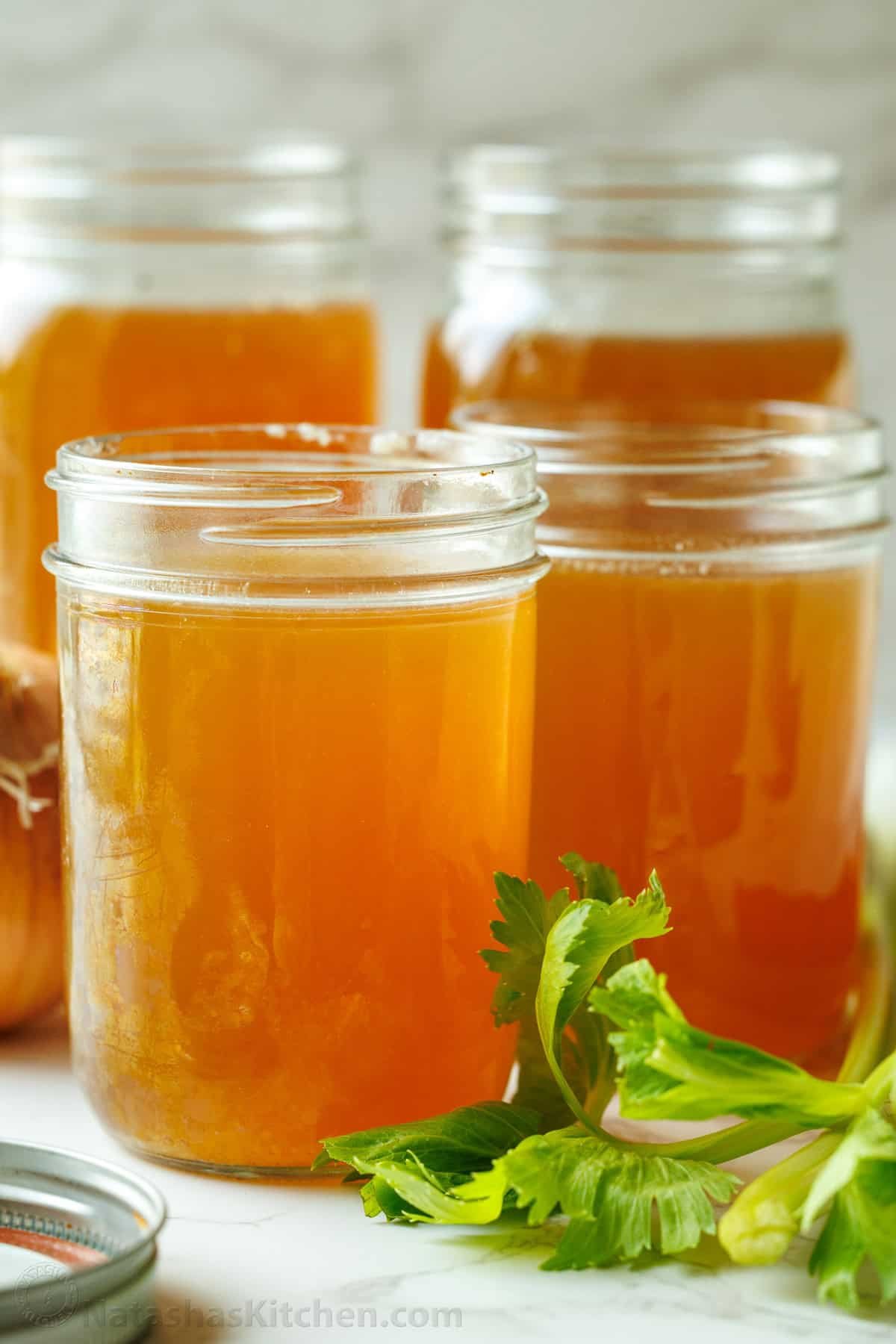 Four mason jars of homemade beef stock with parsley garnish