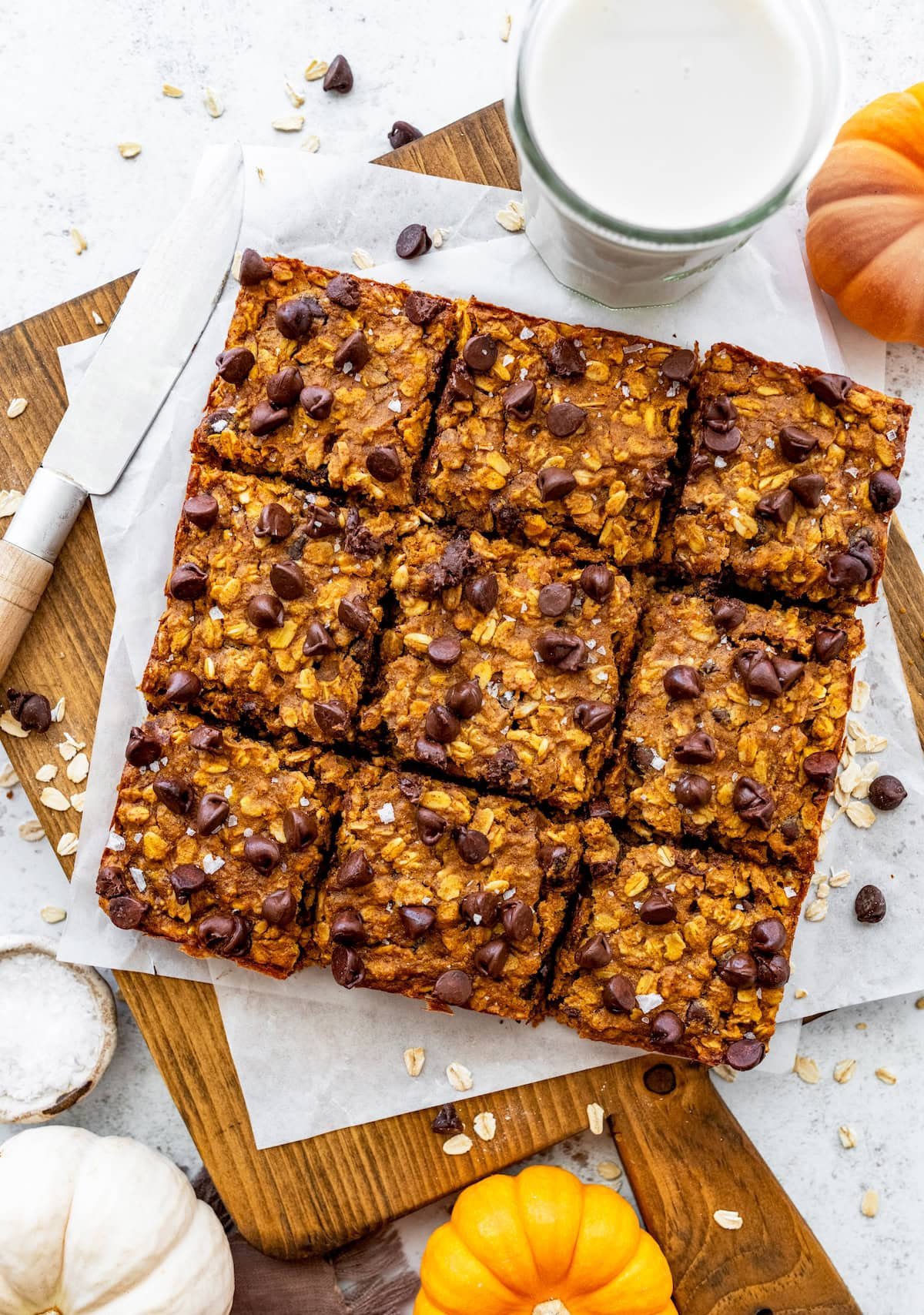 pumpkin chocolate chip oatmeal bars cut into squares on wood board with glass of milk.