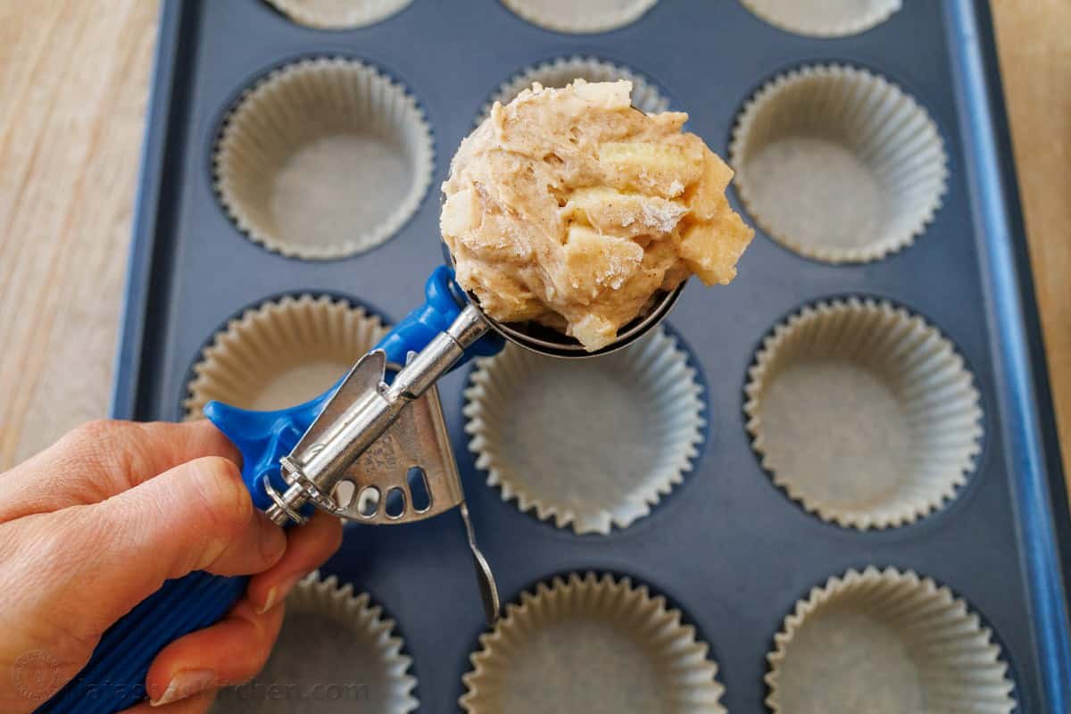 Bakery-style Apple muffins with crumb topping are so easy to make, with a moist crumb and chunks of apple inside. Uses just pantry staples. Ice cream scoop adding batter to a muffin tin with muffin liners