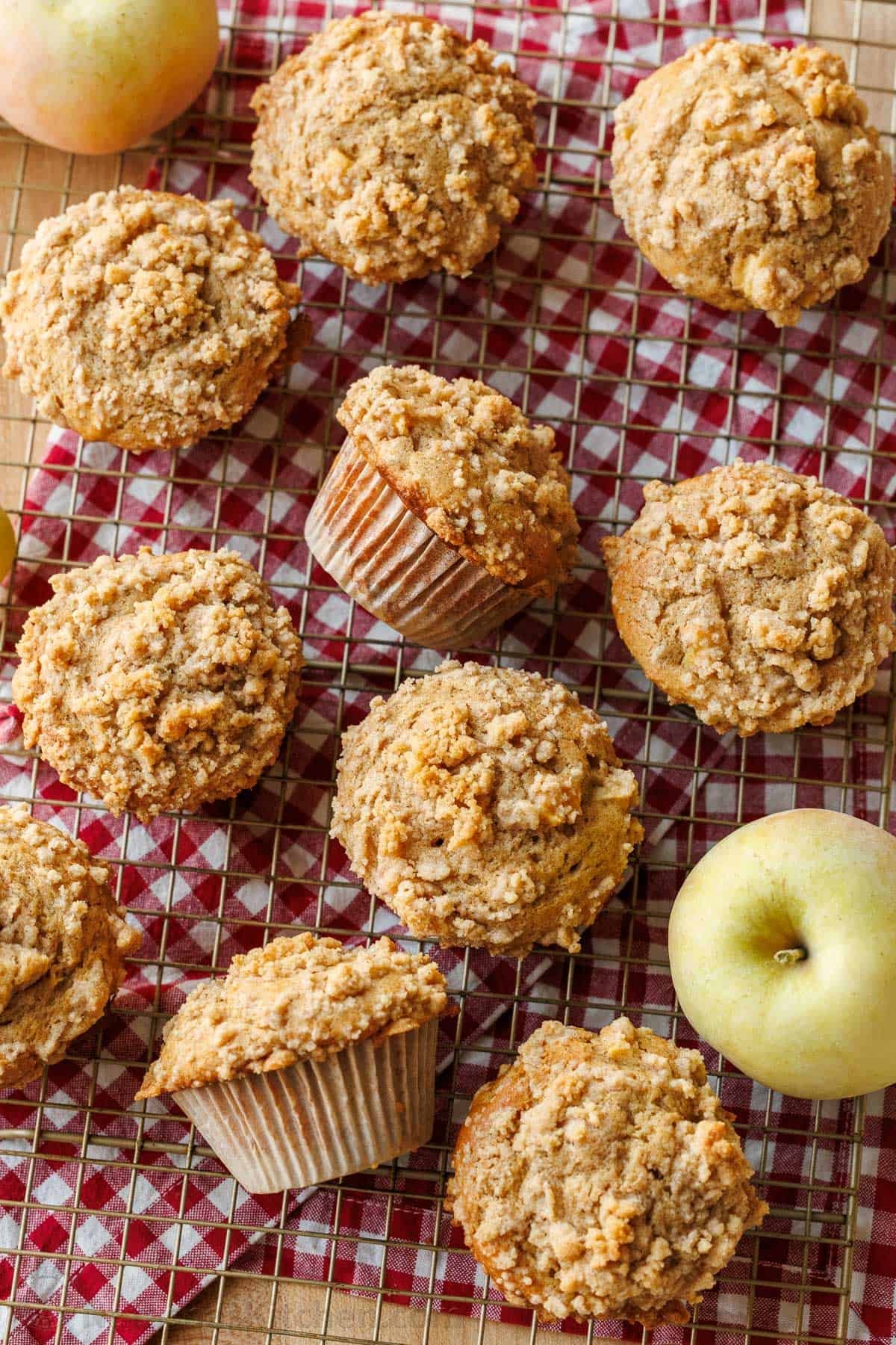 Bakery-style Apple muffins with crumb topping are so easy to make, with a moist crumb and chunks of apple inside. Uses just pantry staples. Apple muffins on a baking rack on a red checkered cloth