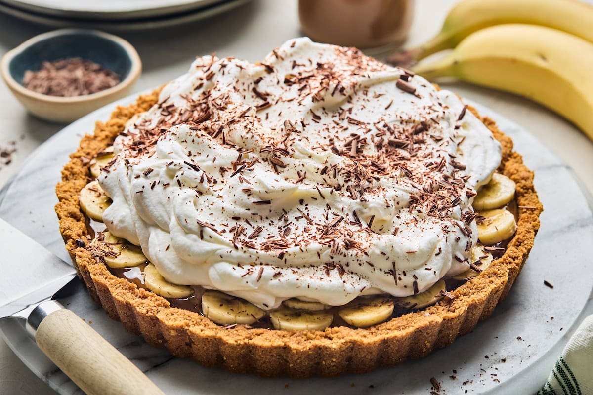 Banoffee pie with whipped cream and chocolate shavings on marble board.
