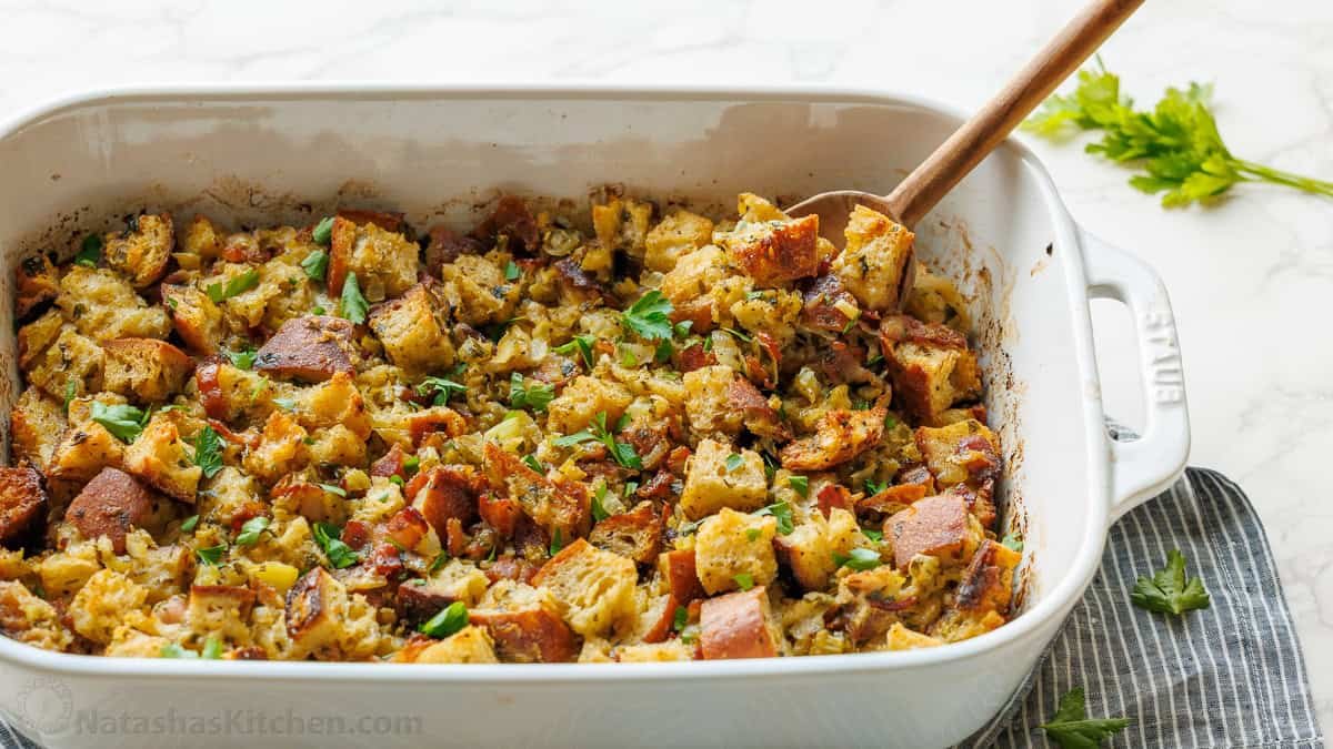 Turkey stuffing recipe baked in a white casserole with a serving spoon