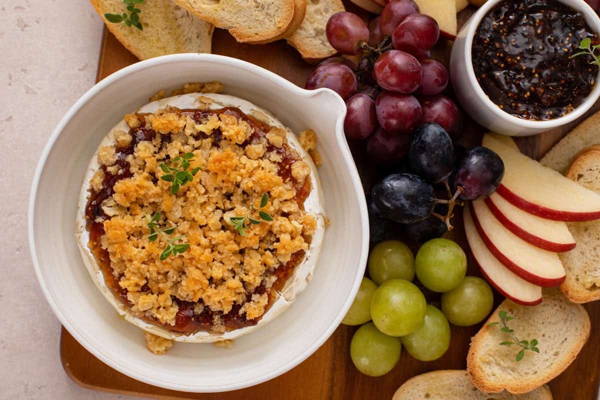 Baking dish holding bake brie with jam arranged on a platter of fruit and baguette slices.