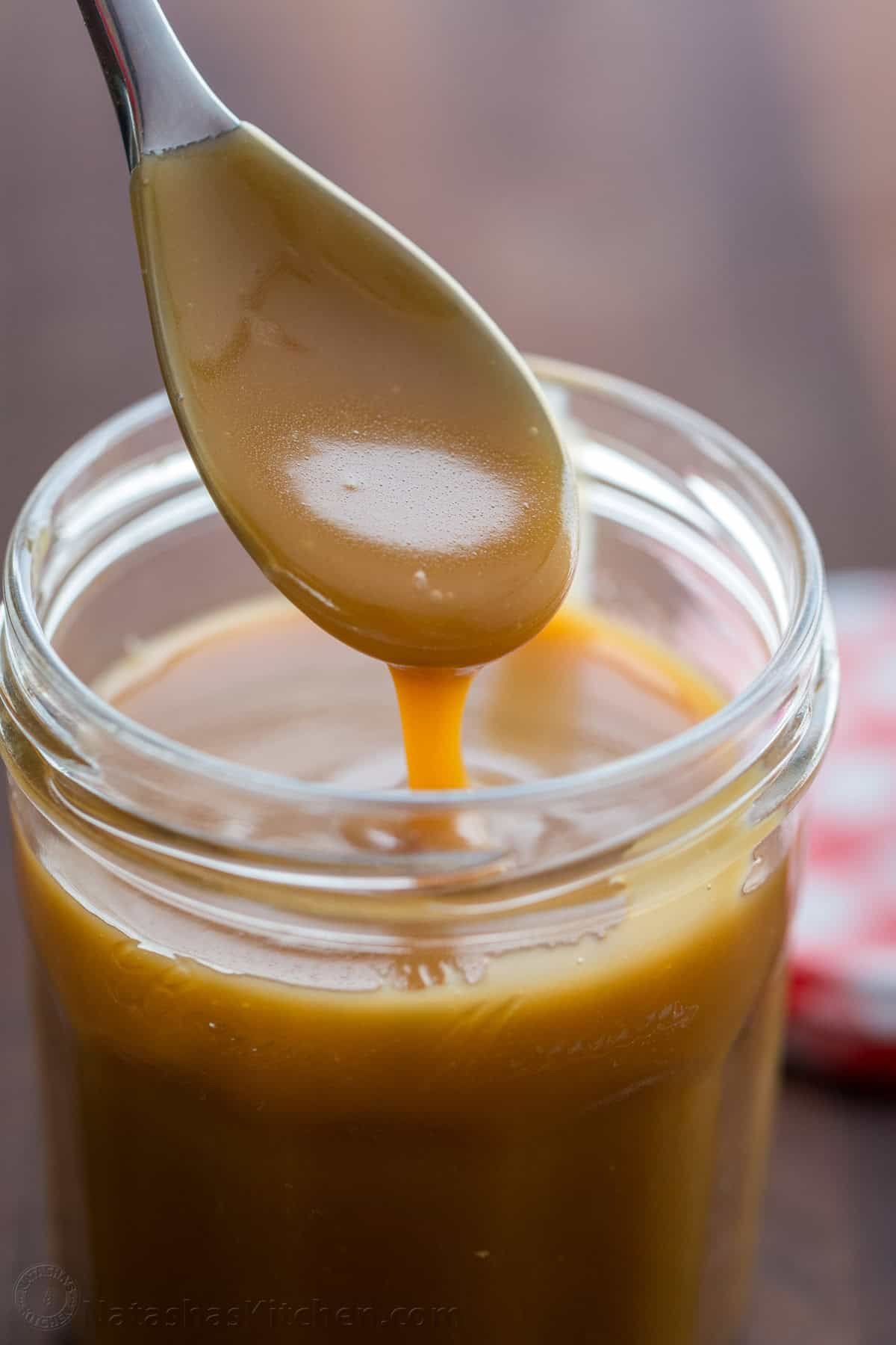 Thick and creamy butterscotch sauce on a spoon dripping into a mason jar