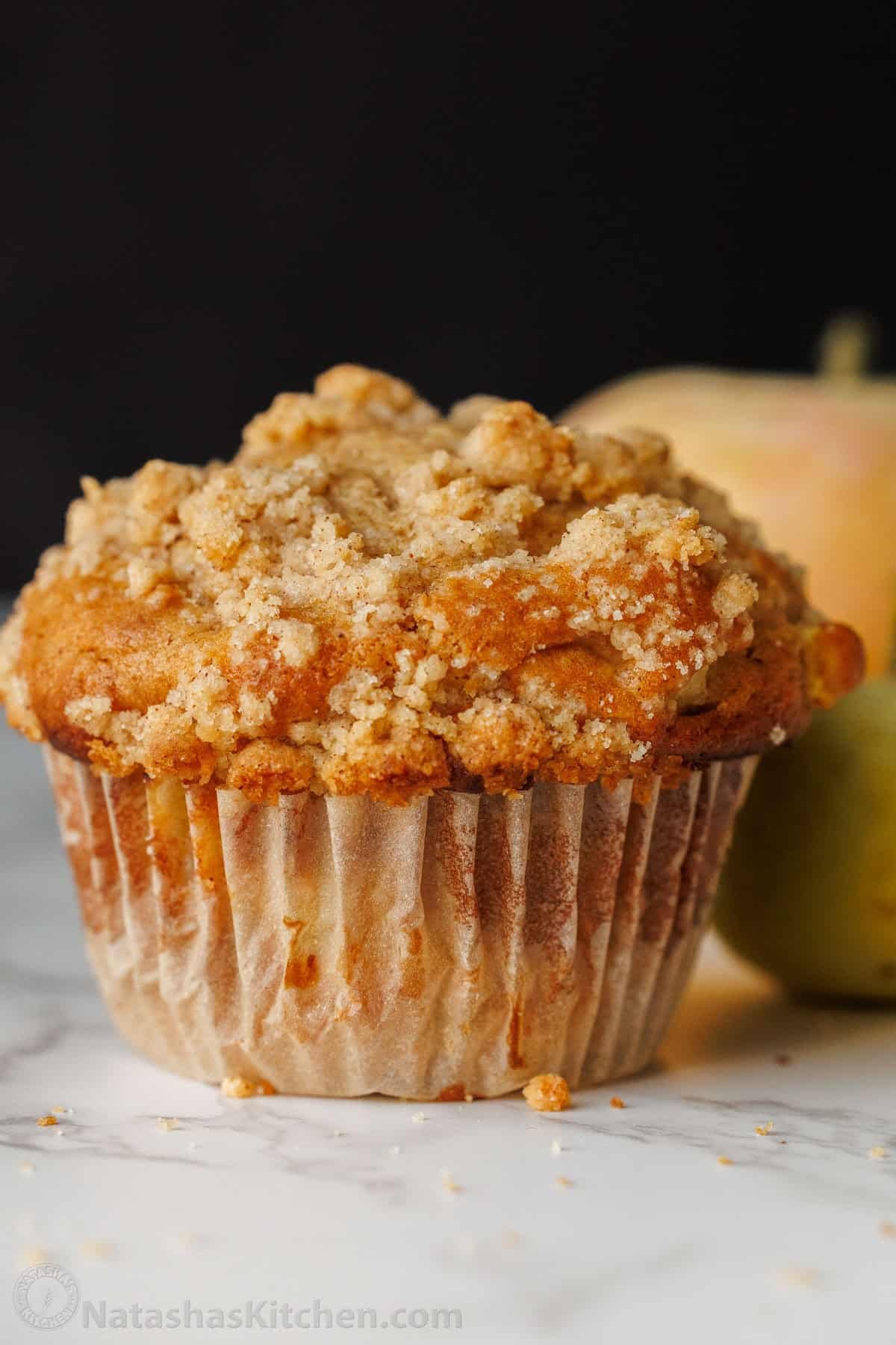 Bakery-style Apple muffins with crumb topping are so easy to make, with a moist crumb and chunks of apple inside. Uses just pantry staples. Apple muffin with crumb topping on a table next to an apple.