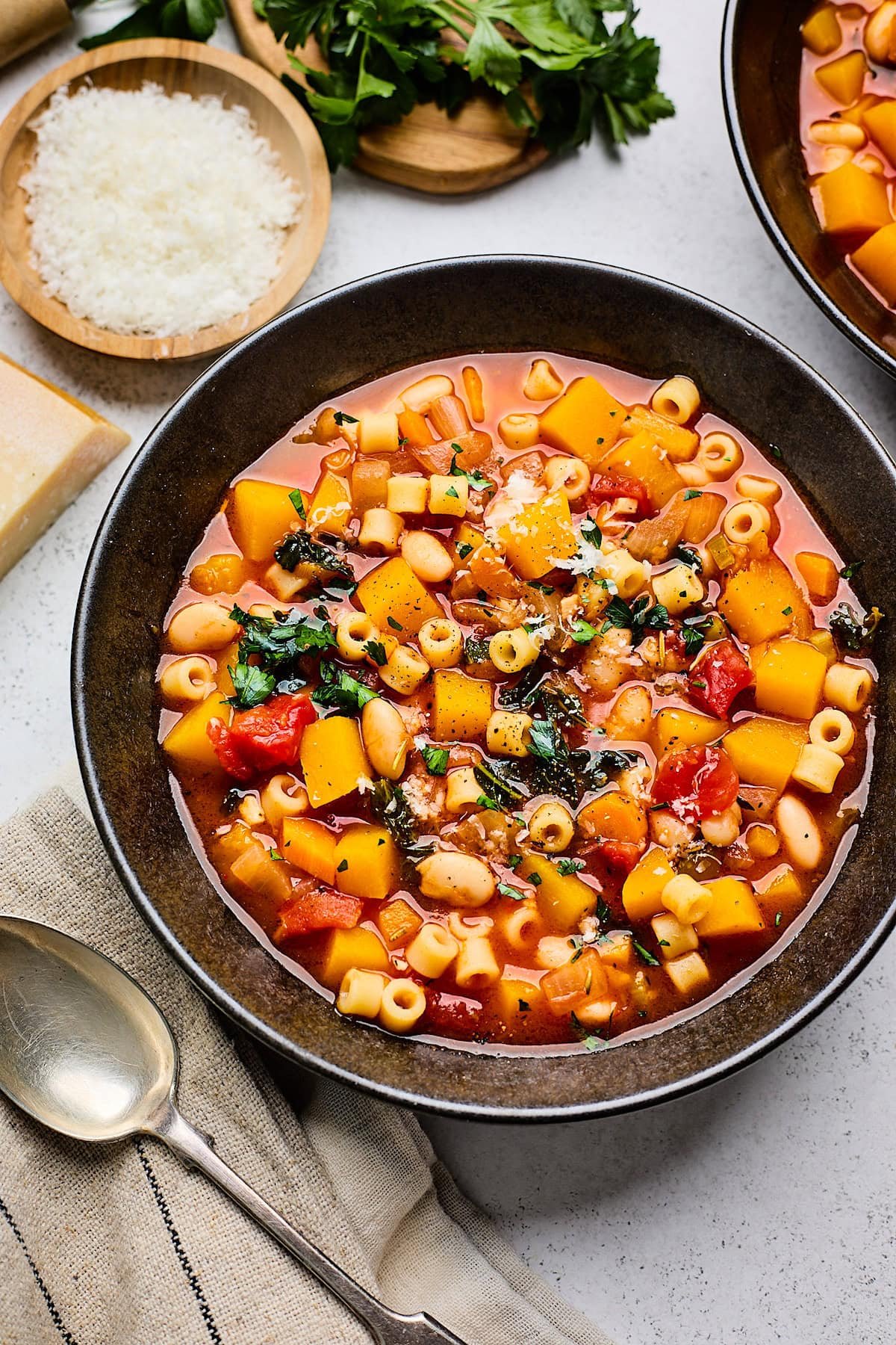 fall minestrone soup in bowl with freshly grated parmesan cheese in little bowl.