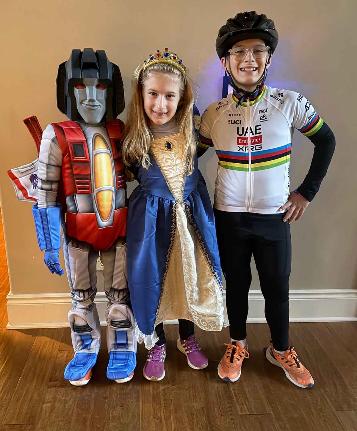 Three kids dressed up for Halloween as a Transformer, a queen, and a cyclist.