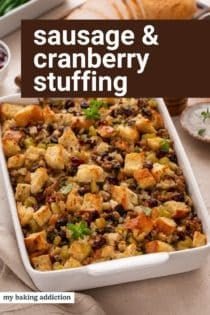 Baked pan of sausage and cranberry stuffing on a countertop. Text overlay includes recipe name.