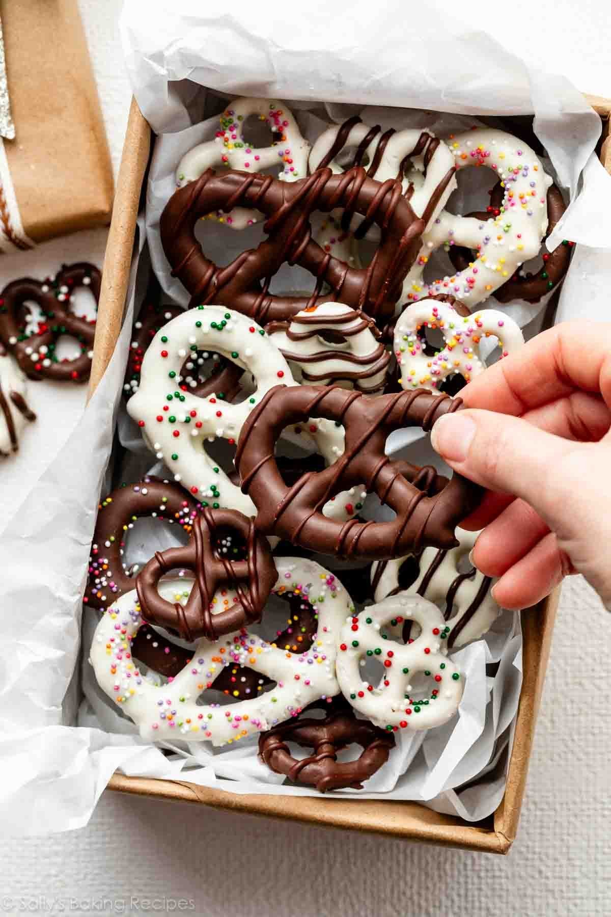 hand grabbing chocolate covered pretzel from lined box.