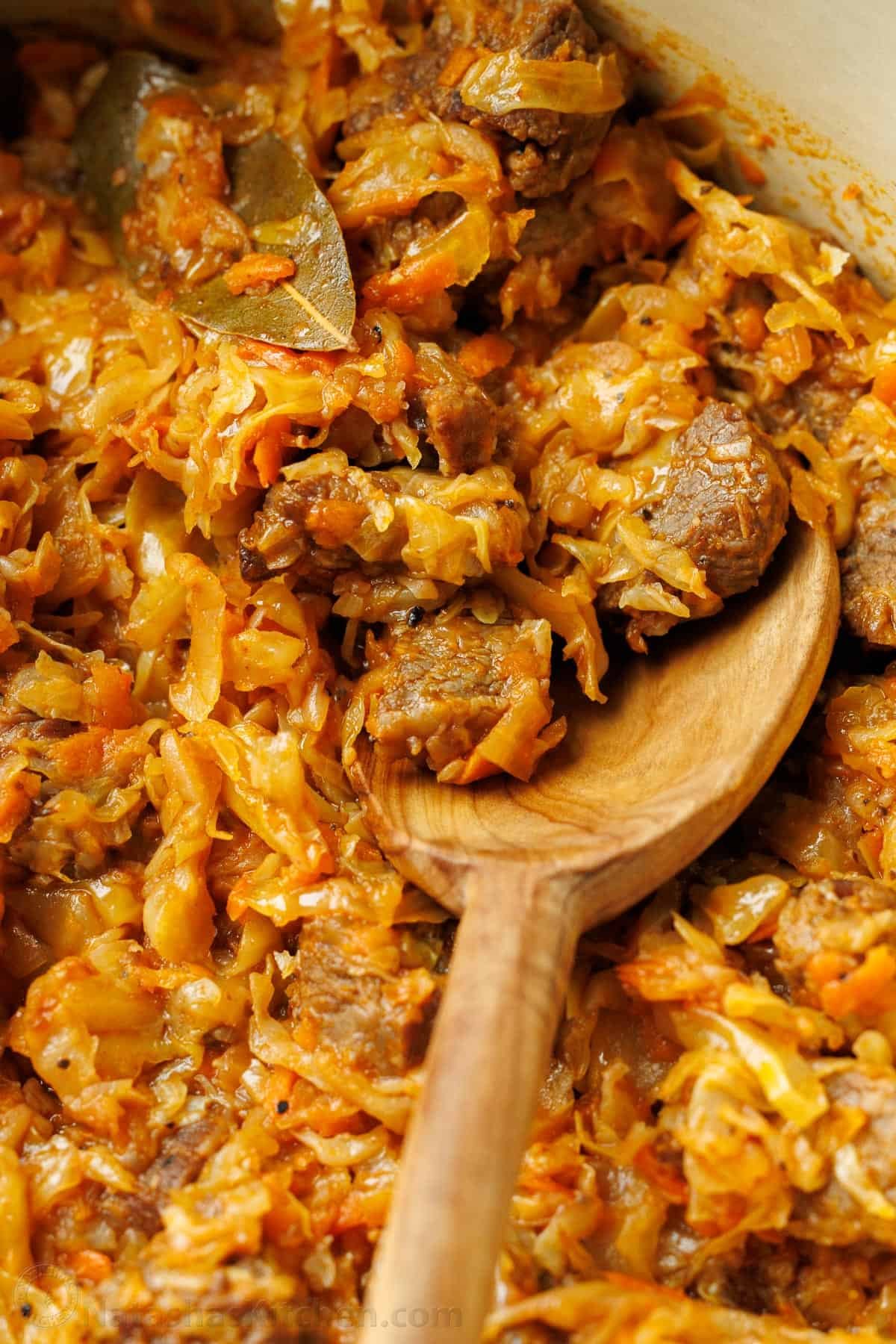 Wooden spoon scooping braised cabbage with beef