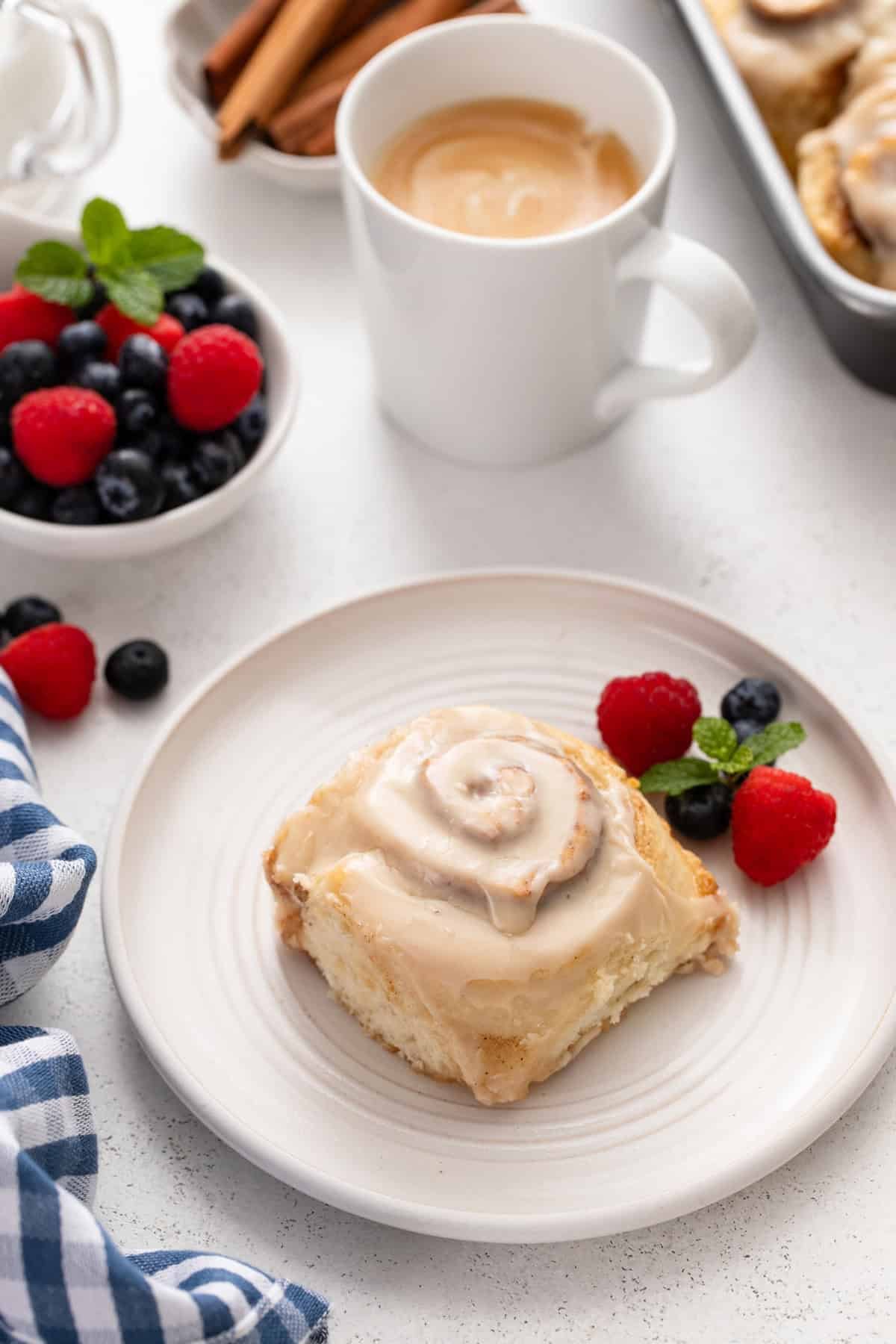 Plated biscuit cinnamon roll with a cup of coffee in the background.