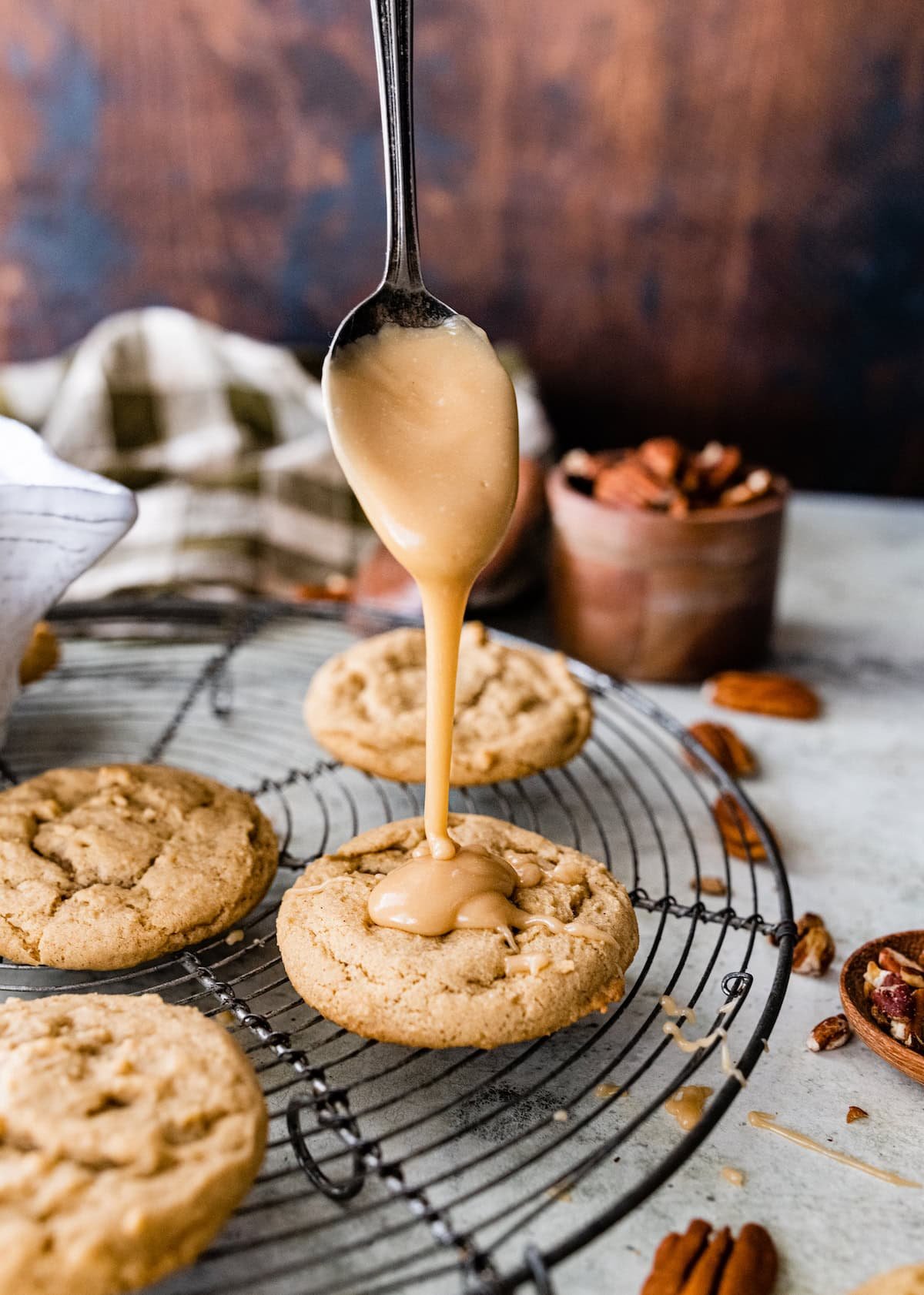 maple glaze being drizzled with a spoon on top of maple pecan cookies on cooling rack.