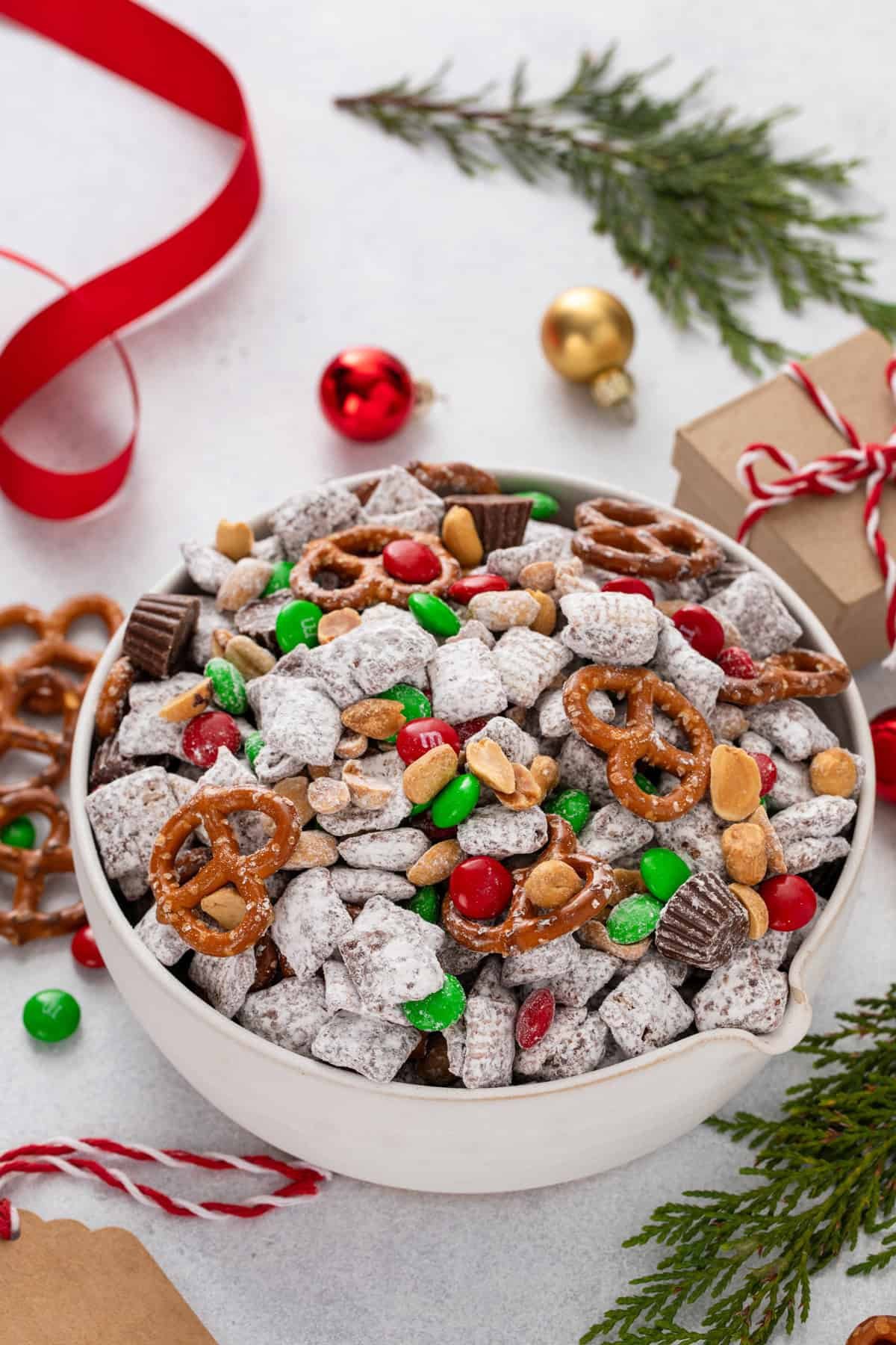 White bowl filled with reindeer chow surrounded by Christmas decorations.