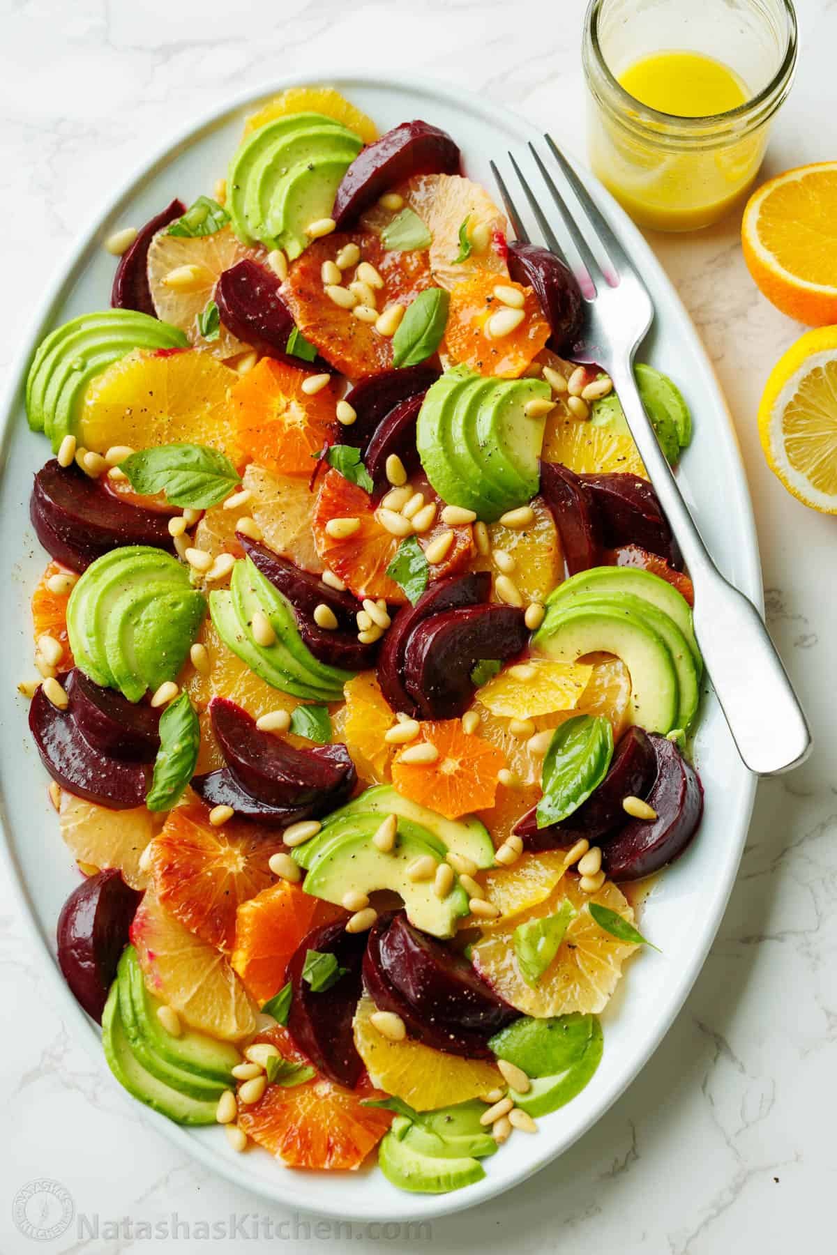 Citrus salad on a white plate with a fork and lemon vinaigrette in a mason jar