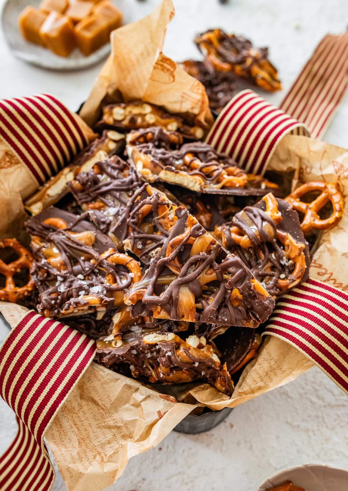 chocolate caramel pretzel bark pieces in a gift box with ribbon. 