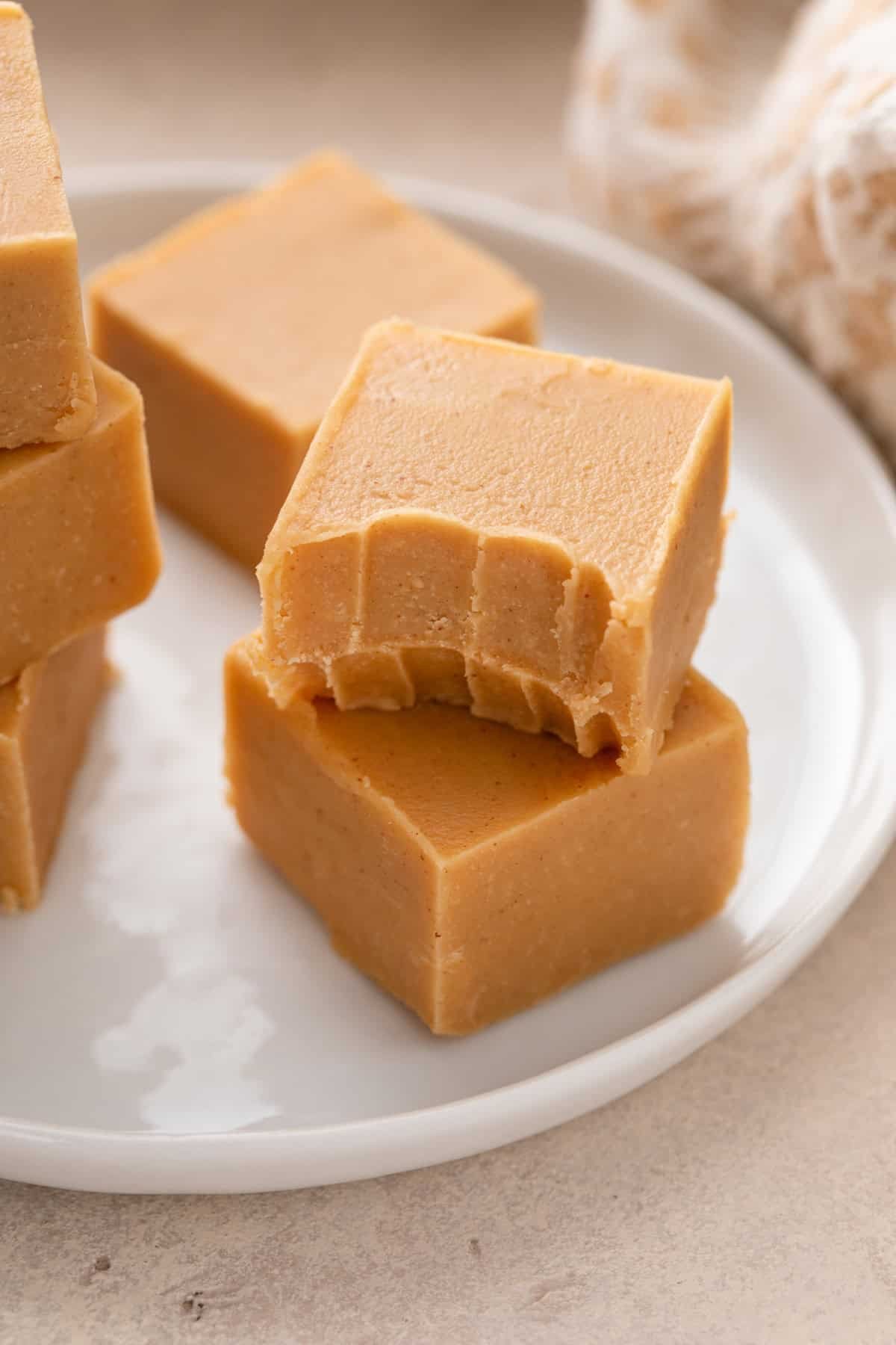 Two pieces of peanut butter fudge stacked on a white plate with a bite taken from the piece of fudge on the top.