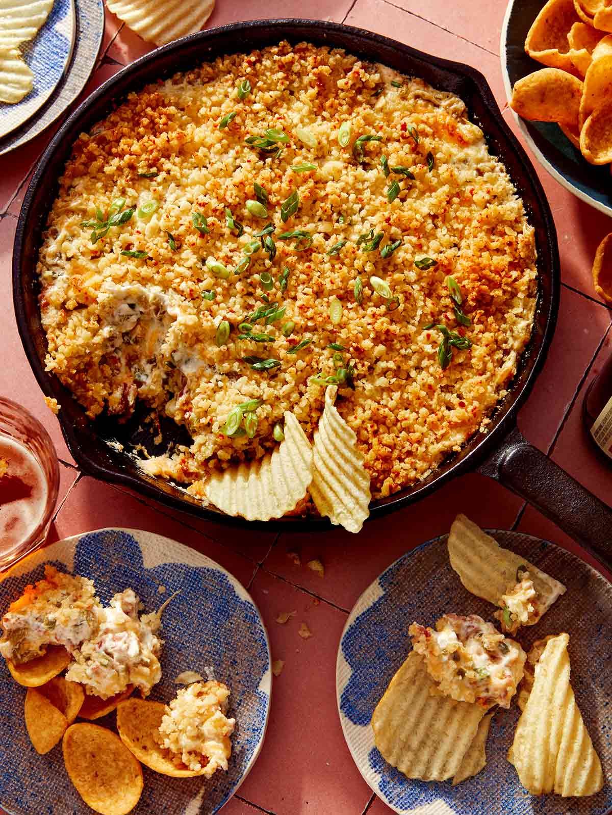 Jalapeño popper dip in a cast iron skillet with chips on the side and being dipped into it.