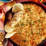 Jalapeño popper dip up close on the skillet with chips and drinks on the side.