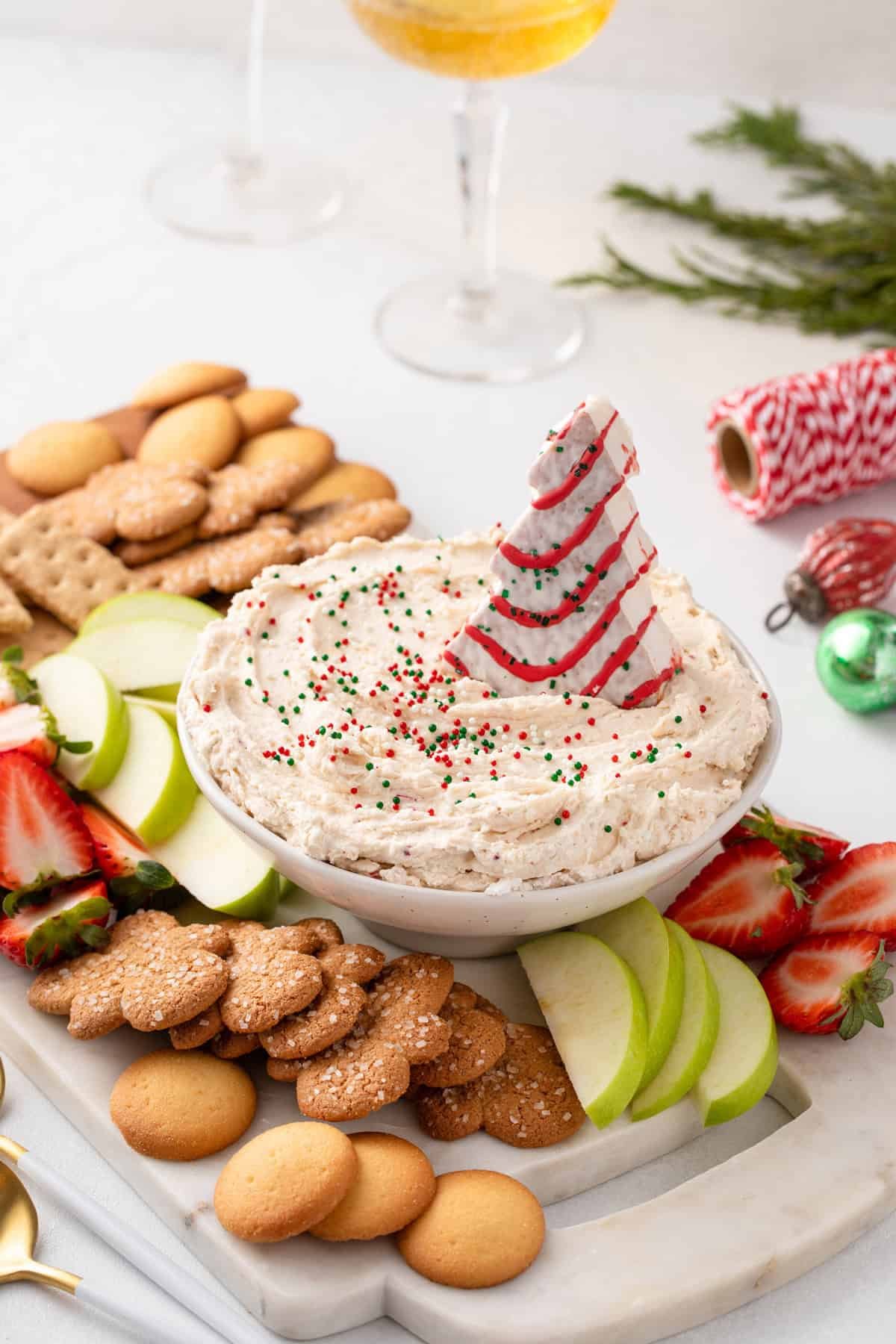 Bowl of christmas tree cake dip on a platter surrounded by cookies and fresh fruit.