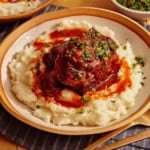 Braised short ribs on top of a bed of mashed potatoes in a bowl.