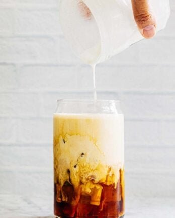 photo of hand pouring a jar of vanilla sweet cream cold foam over a glass of iced coffee