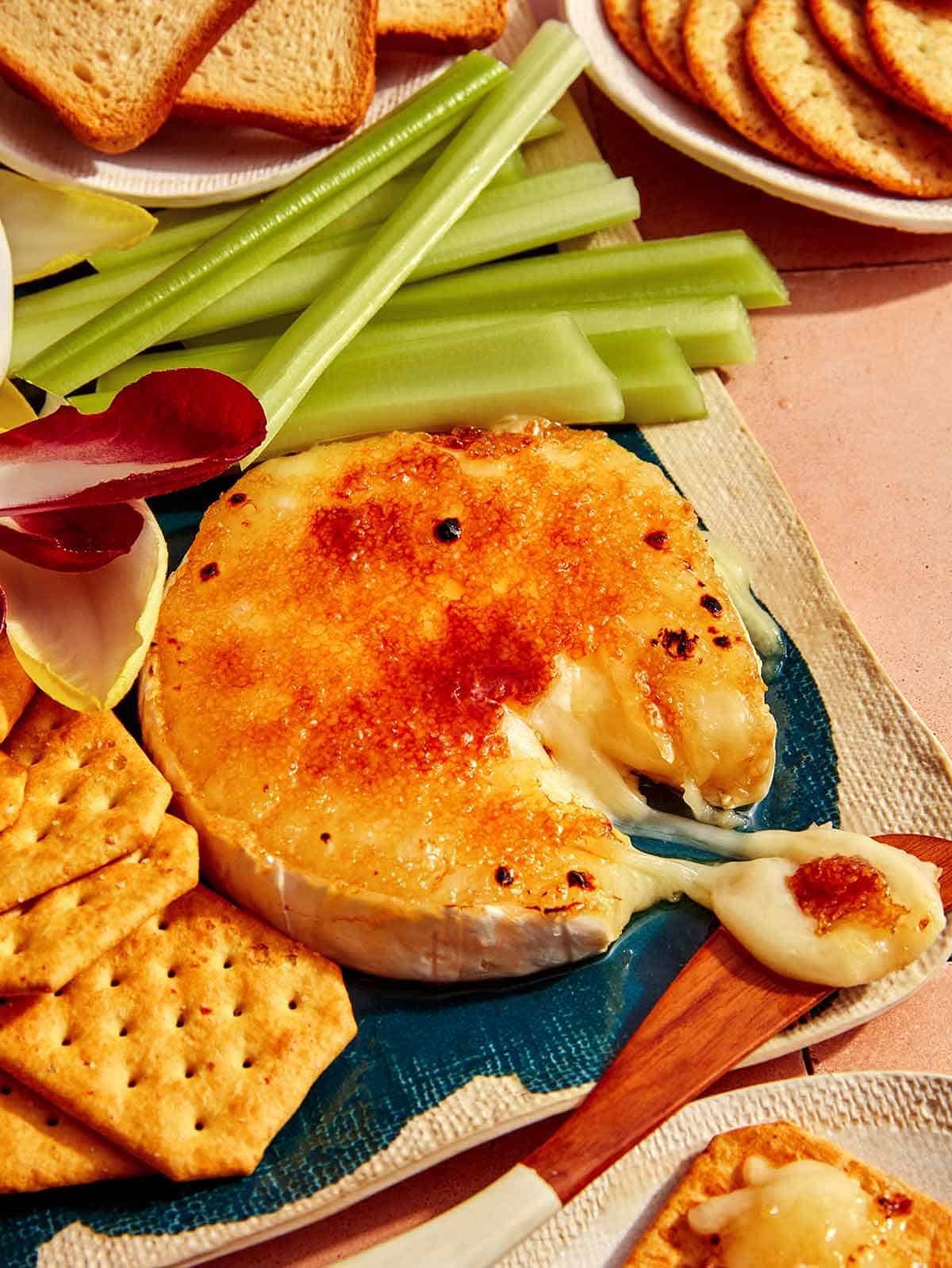 Honey Brûlée Brie on a platter with a knife taking some cheese.