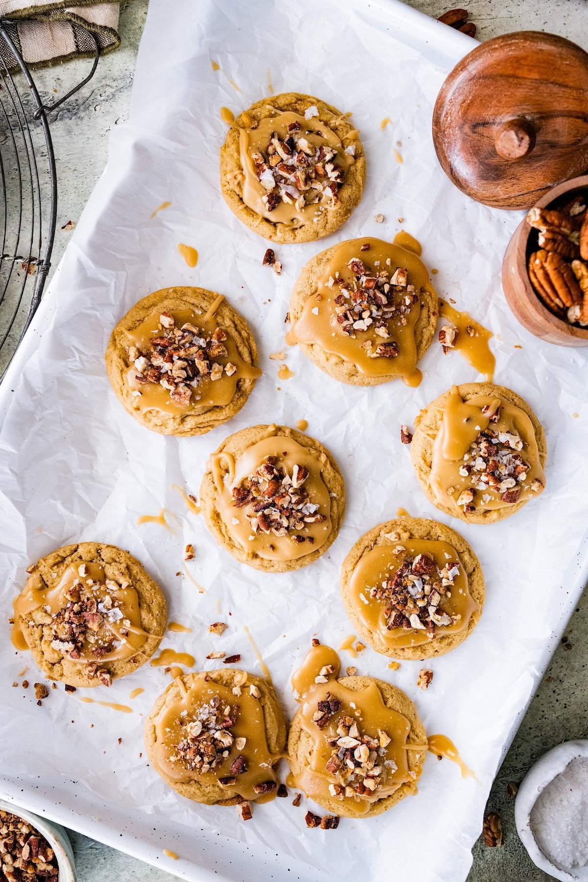 brown sugar maple pecan cookies with maple glaze, chopped pecans, and flaky sea salt on baking sheet with parchment paper.