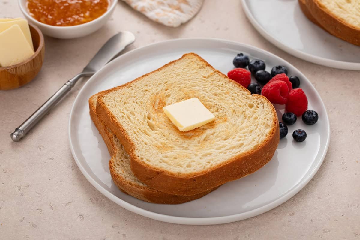 White plate with two slices of toasted potato bread next to fresh berries.