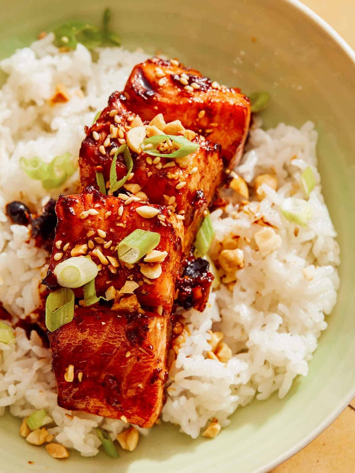 Up close on a piece of salmon with a soy glaze i on top of a bed of rice.