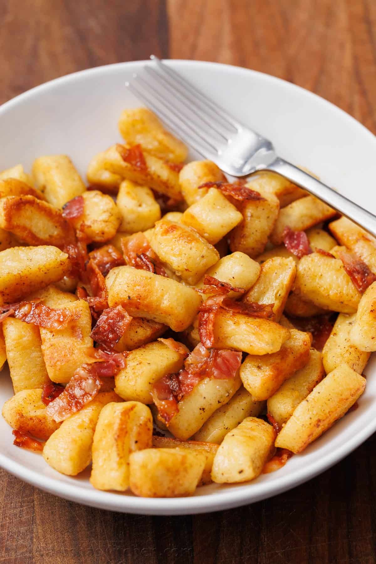 Ricotta Gnocchi satisfy the craving for gnocchi with very little effort. No need to fuss with potatoes since the star ingredient is ricotta cheese. white bowl of homemade ricotta gnocchi with crispy bacon