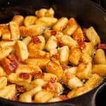 ricotta gnocchi frying in a cast iron pan with bacon bits