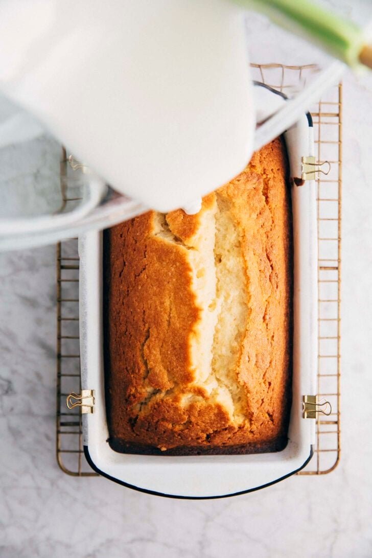 Photo of Michelle from Hummingbird High pouring lemon glaze over the lemon yogurt loaf